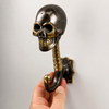 Hand holding solid brass skull coat hook in dark antique finish on neutral background showing skull face spine and hook detail — gothic dark academia skull hook handmade in Bali
