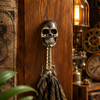 Brass skull wall hook mounted on dark wood wall with bag hanging styled with steampunk clock gears and vintage lantern — gothic skull coat hook handmade in Ubud Bali
