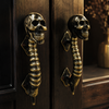 Pair of solid brass skull spine door handles in dark antique finish installed on a dark wood door — gothic skeleton entry hardware double door pull handmade in Ubud Bali