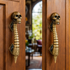 Pair of solid brass skull spine door handles installed on warm wooden double doors with garden light behind — gothic brass double door pull handmade in Bali
