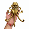 Hand holding a brass skull-octopus wall hook in a polished gold finish, showing hand cast detail