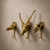 Set of 3 antique brass animal skull wall hooks displayed on a clean neutral wall showing crocodile dinosaur and impala designs — handmade skull hook set Ubud Bali