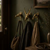Three brass skull wall hooks on a dark green wall with bags hanging in a gothic dark academia interior — animal skull wall hook set handmade in Bali
