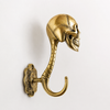 Small solid brass skull wall hook in polished gold finish on a neutral background showing full sculptural skeleton figure skull face and single curved hook — gothic skull hook clearance handmade in Bali