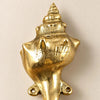 Close-up of the brass spiral conch shell hook, showing the hand-cast ridges of the spiral shell and the two screw loops for wall mounting. Handmade cast brass coastal wall hook from Ubud, Bali.