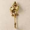 Brass spiral conch shell wall hook mounted on a warm beige wall, with a ridged spiral shell on top and a long stem ending in a ball-tipped hook. Handmade cast brass seashell towel and coat hook, hand-finished by artisans in Ubud, Bali.