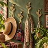 Set of brass sprout leaf hooks mounted on a green wall holding a woven hat, scarves, and patterned bags