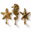 Brass starfish and seahorse wall hook set of 3 on a white background: a pebbled starfish hook, a seahorse hook with curled tail and a slim textured starfish hook, each with a ball-tipped hook. Handmade cast brass nautical wall hooks, hand-cast and finished by artisans in Ubud, Bali.