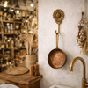 Handmade brass sunflower wall hook used as a pan hanger in a boho cottagecore kitchen with wooden shelves and vintage cookware.