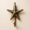 Brass textured starfish wall hook mounted on a warm beige wall, with finely detailed sea star arms, a top screw loop and a ball-tipped hook below. Handmade cast brass sea star towel and coat hook from Ubud, Bali, part of the brass starfish and seahorse wall hook set of 3.