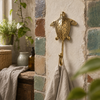 Brass sea turtle wall hook mounted on a rustic tiled wall holding a towel, handmade coastal nautical bathroom decor.