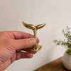 Hand holding brass whale tail wall hook showing size and detail, solid brass coastal wall hook