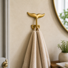 Solid brass whale tail wall hook used as bathroom towel hook in coastal decor, minimal nautical wall styling