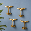 Set of brass whale tail wall hooks on a blue wall for coastal nautical decor styling. Beach house wall hooks for towels, entryway storage, or decorative accents