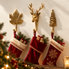 Three brass woodland wall hooks, a maple leaf, a deer head and a pine tree, holding red velvet Christmas stockings filled with gifts, with warm Christmas tree lights glowing behind. A festive stocking holder set and Christmas gift for rustic cabin and holiday wall decor, handmade in Bali.