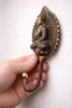 Angle view of brass Buddha wall hook in hand showing hook depth and functionality