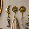 Three celestial brass wall hooks mounted on warm neutral wall holding keys linen towel and beaded chain – crescent moon hook sun and moon face hook and sun wall hook in polished gold – boho witchy celestial entryway bathroom decor – astrology housewarming gift – solid brass Bali artisan
