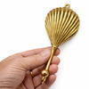 Brass clam shell wall hook held in hand showing size and shell detail