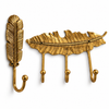 Gold brass feather wall hook set of 2 on a white background: one single feather hook and one 3-hook feather coat rack in a bright polished gold brass finish. Handmade cast brass boho wall hooks for coats, towels, bags and keys, hand-cast and finished by artisans in Ubud, Bali.