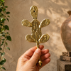 Close-up of a hand holding a single handcrafted brass cactus wall hook, showing the solid brass texture and artisan finish made in Bali