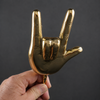 Close-up of a hand holding a brass hand gesture wall hook, showing the solid brass texture of this rock on coat hook.
