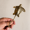 Close-up of a hand holding a handcrafted brass sea turtle wall hook, showing the solid brass texture from the set of 4.