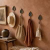 Row of brass and bronze leaf wall hooks holding a hat, bag, and towel on a terracotta entryway wall
