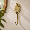 Minimalist brass monstera leaf wall hook mounted on wall, modern botanical home decor accent