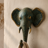 Close-up of patina brass elephant wall hook mounted on warm neutral wall with natural linen cloth hanging showing rich verdigris patina finish, intricate trunk detail and golden tusk and ear accents. Handcrafted decorative coat hook and towel hook from set of 4 for boho home decor, wabi sabi decor, yoga room decor and eclectic gallery wall. Unique boho housewarming gift set of 4