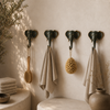 Patina brass elephant wall hooks mounted on dark moody boho wall with natural accessories showing dramatic eclectic interior styling and rich verdigris patina finish with golden tusk detail. Handcrafted decorative coat hook set and towel hook set from set of 4 for boho home decor, wabi sabi decor, yoga room decor and meditation space decor. Unique boho housewarming gift gallery wall hook set