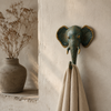 Patina brass elephant wall hook mounted on warm neutral wall beside dried pampas grass and natural linen cloth showing wabi sabi boho interior lifestyle styling. Handcrafted verdigris patina elephant decorative coat hook and towel hook from set of 4 for boho home decor, wabi sabi decor, yoga room decor and eclectic gallery wall. Unique boho housewarming gift and meditation space decor set
