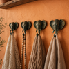 Set of four patina brass elephant wall hooks mounted on warm terracotta boho wall with natural linen towels, macrame bead strand and knitted textile hanging showing complete wabi sabi gallery wall lifestyle styling. Handcrafted verdigris patina elephant coat hook set and towel hook set for boho housewarming gift, yoga room decor, meditation decor and eclectic gallery wall decor. Unique wabi sabi home gift set of 4 with no tariffs for US buyers.
