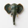 Slightly angled front view of patina brass elephant wall hook on white background showing full verdigris patina finish, detailed trunk sculpture, golden tusk and warm gold ear accents with hook mounted below. Handcrafted decorative coat hook and towel hook from set of 4 for boho home decor, wabi sabi decor, yoga room and meditation space decor. Unique boho housewarming gift set of 4