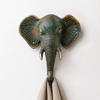 Patina brass elephant wall hook isolated on white background showing full verdigris patina finish, intricate trunk detail, golden tusk accents, warm gold ear detail and single hook below. Handcrafted decorative coat hook and towel hook from set of 4 for boho home decor, wabi sabi decor, yoga room decor and eclectic gallery wall. Unique boho housewarming gift set of 4