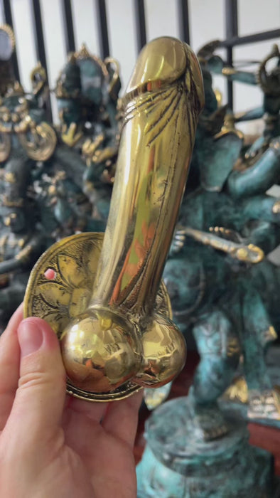 Handheld close-up of 6 inch brass penis cabinet pull and wall hook for scale, artisan-made novelty decor hardware