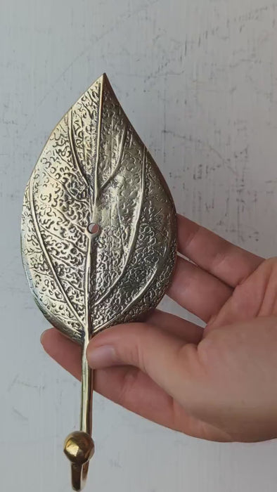 Video showing a handcrafted brass leaf wall hook held in hand, highlighting the hand-cast vein texture and boho botanical design.