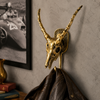 Solid brass impala skull wall hook mounted beside framed artwork on a neutral wall with dark coat hanging — gothic dark academia african animal wall hook handmade in Ubud Bali