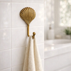 Single brass clam shell wall hook holding a towel in a coastal bathroom setting