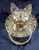 Real front-view photo of the brass cat door knocker on dark blue fabric, showing the detailed cat face, ornate Victorian scrollwork and solid brass ring. A handmade gothic door knocker and animal towel ring, cast from recycled brass in Bali.