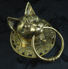 Unedited photo of the brass cat head towel ring at an angle on dark fabric, showing the sculpted cat face, pointed ears, ornate scrollwork plate and solid brass ring. A genuine handmade animal towel ring and cat door knocker from Bali.