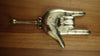 Top-down view of a brass hand gesture wall hook on wood, showing the full sign of the horns hand and hook detail.