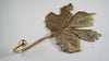 Side angle view of brass maple leaf hook in an antique patina finish showing the curved hook