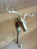 A brass moose-shaped wall sculpture hook with a gold finish, mounted on a wooden surface.