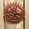 Angled view of hand carved wooden Om wall hanging on rustic wooden surface showing natural wood grain texture and deep relief om symbol carving detail – solid wood om wall decor – yoga meditation spiritual home decor – boho hindu buddhist wall art – made in Bali