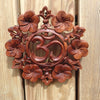 Hand carved wooden Om wall hanging with decorative floral border carving on wooden surface – showing intricate Balinese carving detail and natural wood finish – yoga meditation spiritual boho home decor – unique custom om symbol wall art – made in Bali UbudGlassandBrass