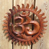 Front view of hand carved wooden Om wall hanging on warm wooden surface showing bold om symbol and sunburst border relief in rich brown wood tone – yoga meditation spiritual home decor – boho hindu om wall decor – meaningful housewarming yoga gift – made in Bali
