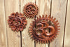 Two hand carved wooden Om wall hangings displayed on wooden surface with tropical flowers showing size comparison and natural wood grain detail – small and medium om symbol wall decor – yoga meditation spiritual boho home decor – handcrafted in Bali Indonesia